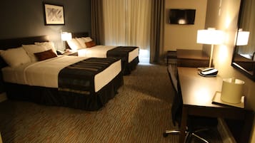 A hotel room with two beds, a desk, a chair, a lamp, a television, and a large mirror.