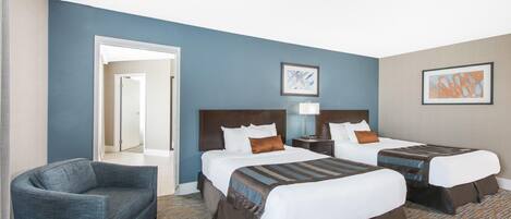A hotel room with two beds, a chair, and a door leading to another room.