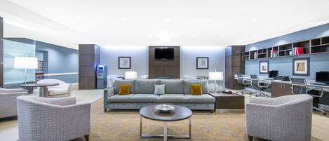A modern lobby with a sofa, armchairs, a coffee table, a TV, and a reception desk.