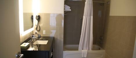 A bathroom with a sink, mirror, hairdryer, and a shower with a curtain.