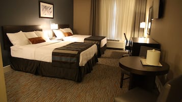 A hotel room with two beds, a desk, a chair, a lamp, and a television.