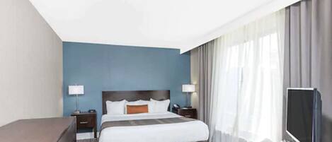 A hotel room with a large bed, a desk, a TV, and a window with curtains.