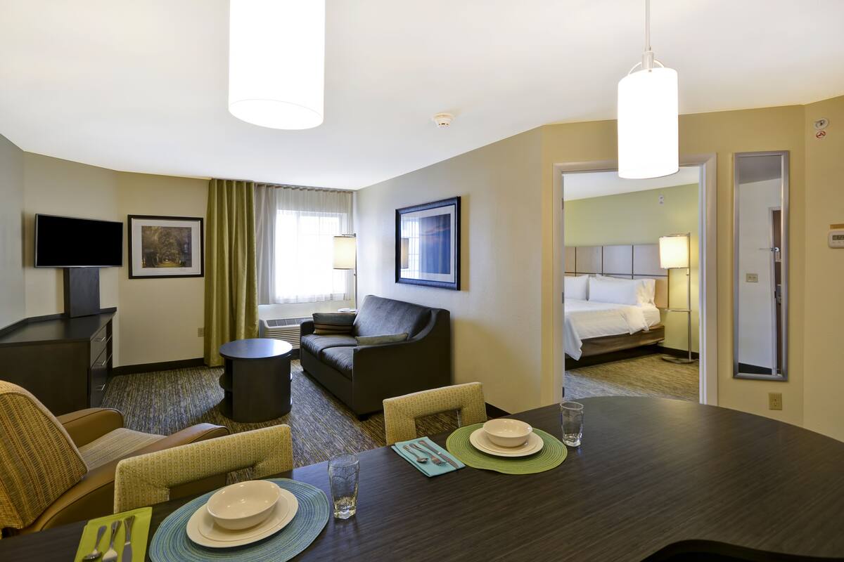 Une chambre d’hôtel comprenant un coin repas, un espace salon avec un canapé et des fauteuils, une télévision et un lit.