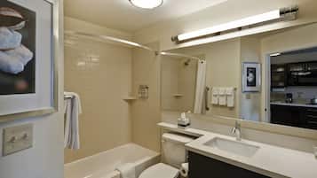 A modern bathroom with a white bathtub, toilet, and sink, a large mirror, and a framed picture on the wall.