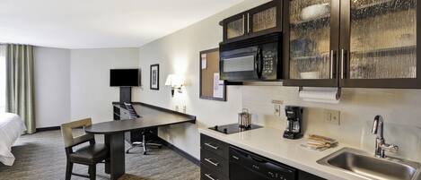 A compact hotel room with a kitchenette, a dining area, and a bed.