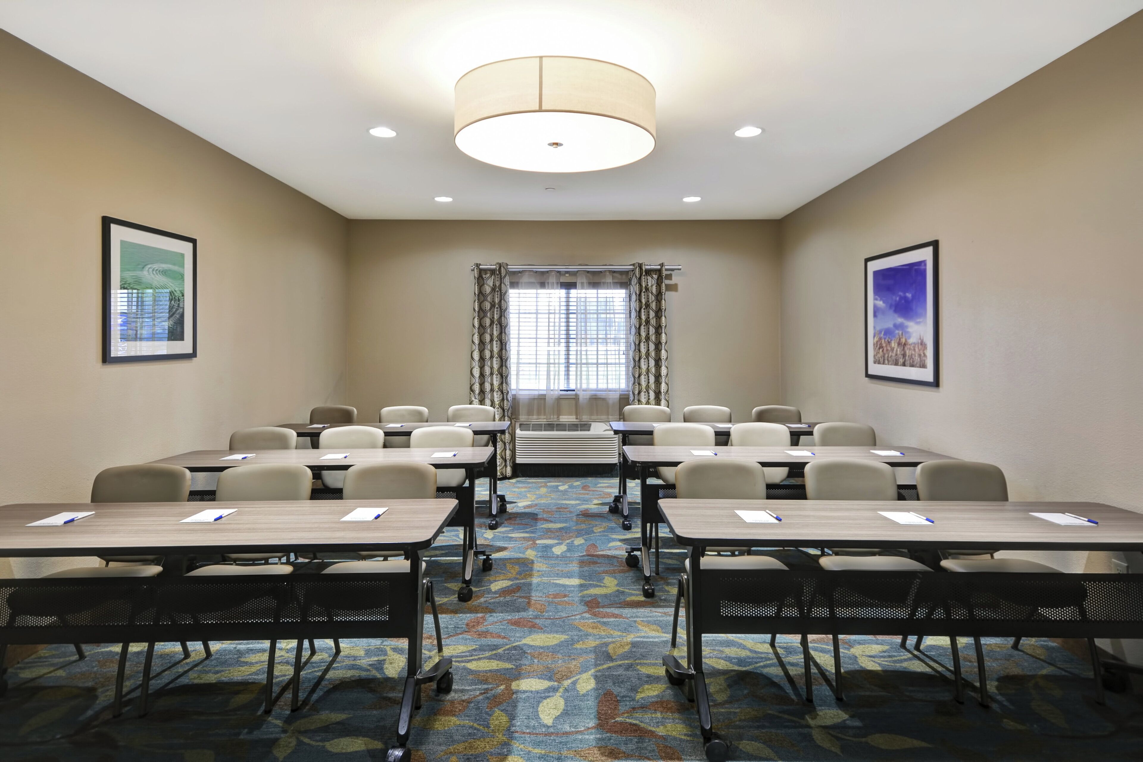 A conference room with tables, chairs, a patterned carpet, and two framed pictures on the walls.