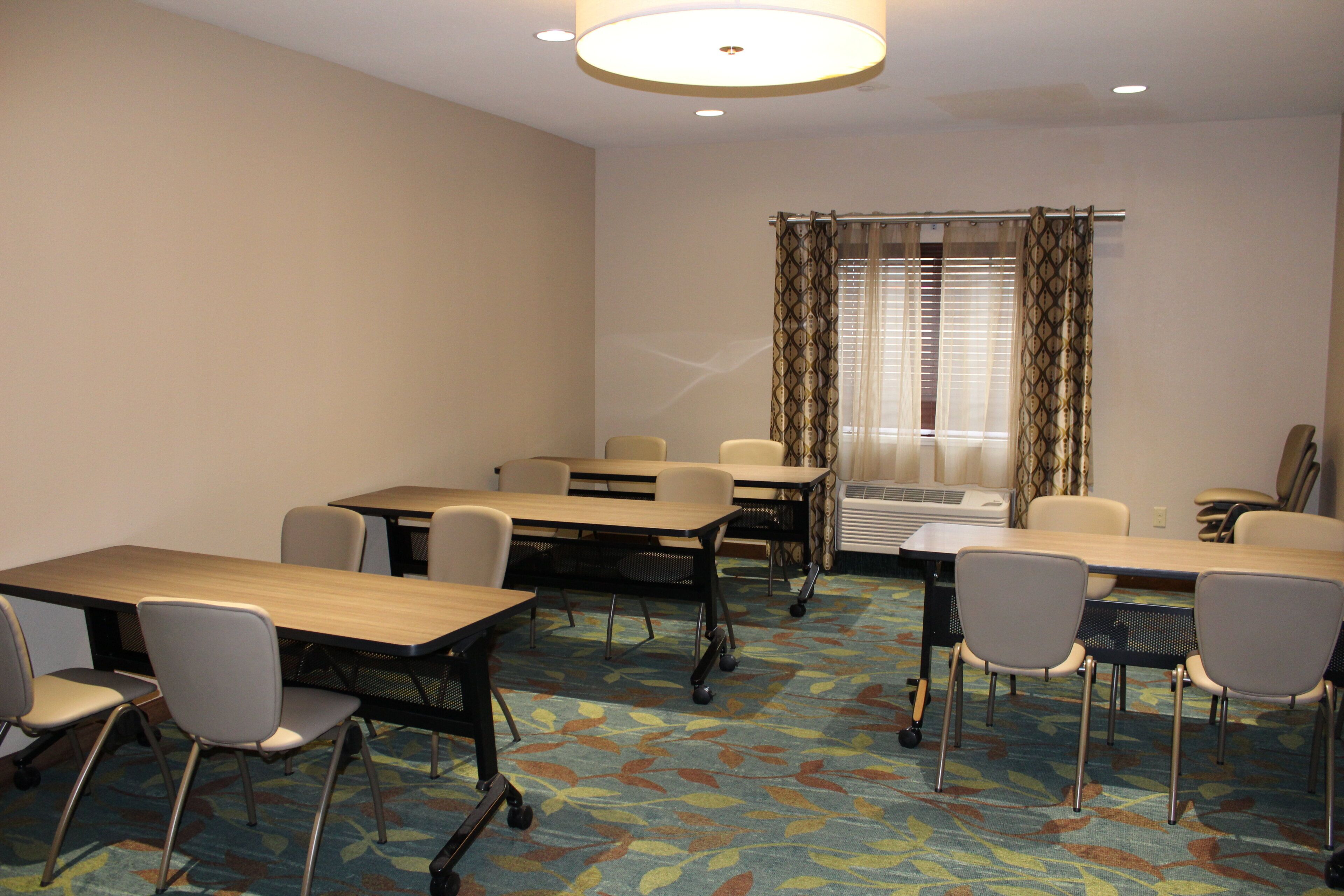 A conference room with tables and chairs, a patterned carpet, and a window with curtains.
