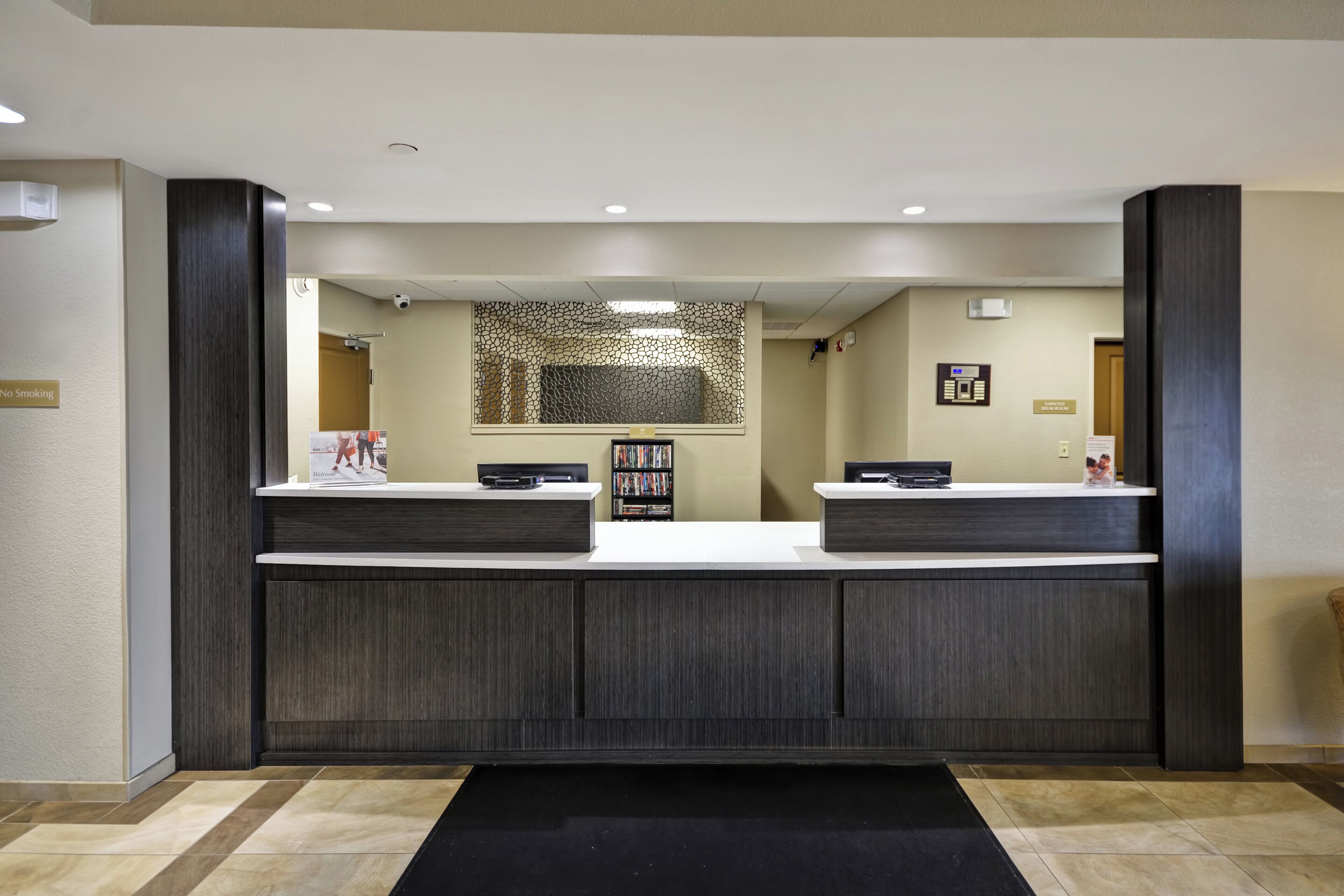 A reception area with a dark wood reception desk, a security camera, and a 'No Smoking' sign.