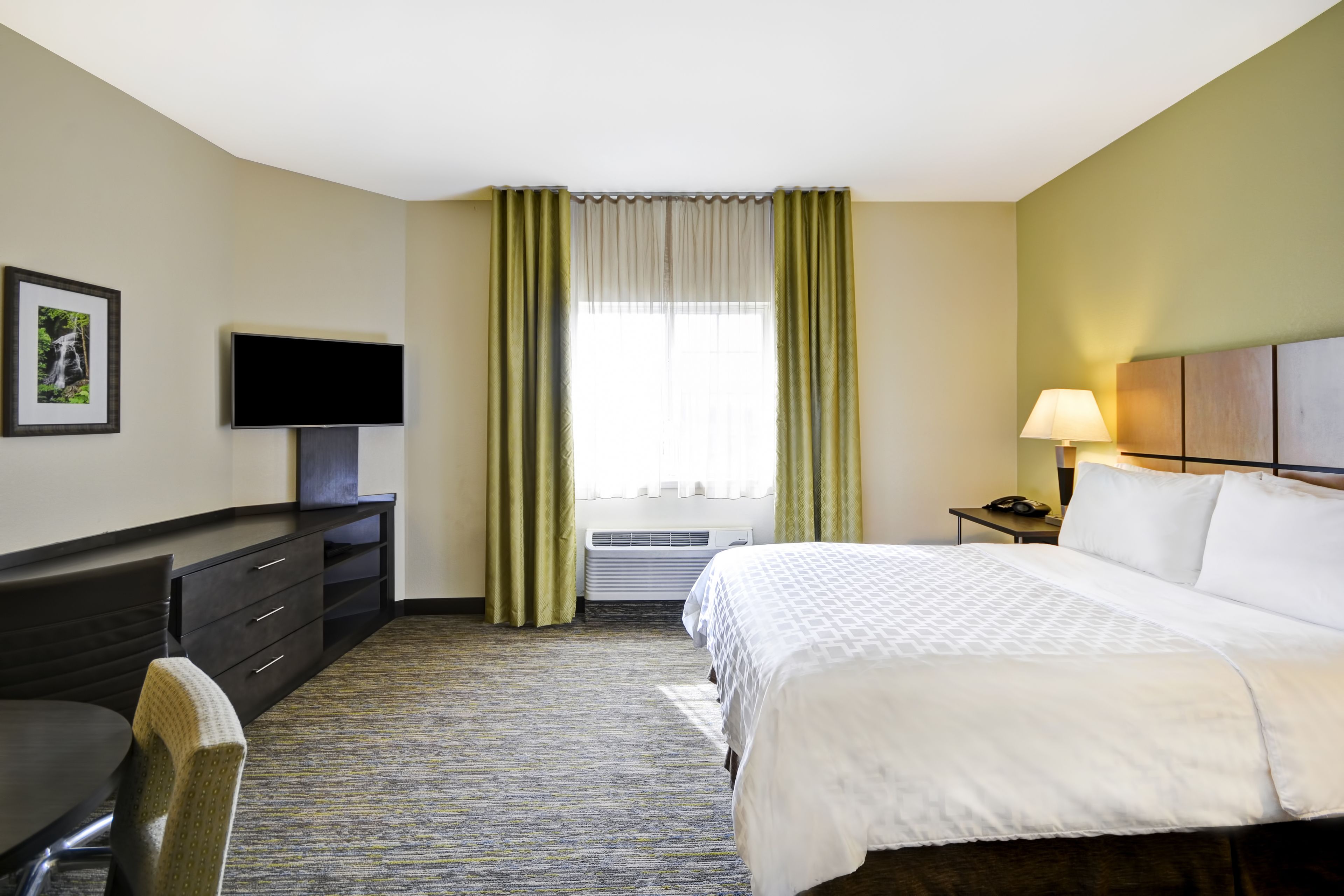A hotel room with a bed, a desk, a chair, a television, a lamp, and a picture on the wall.