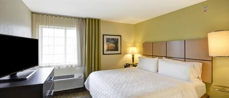 A hotel room with a bed, a TV, a desk, a lamp, and a window with curtains.