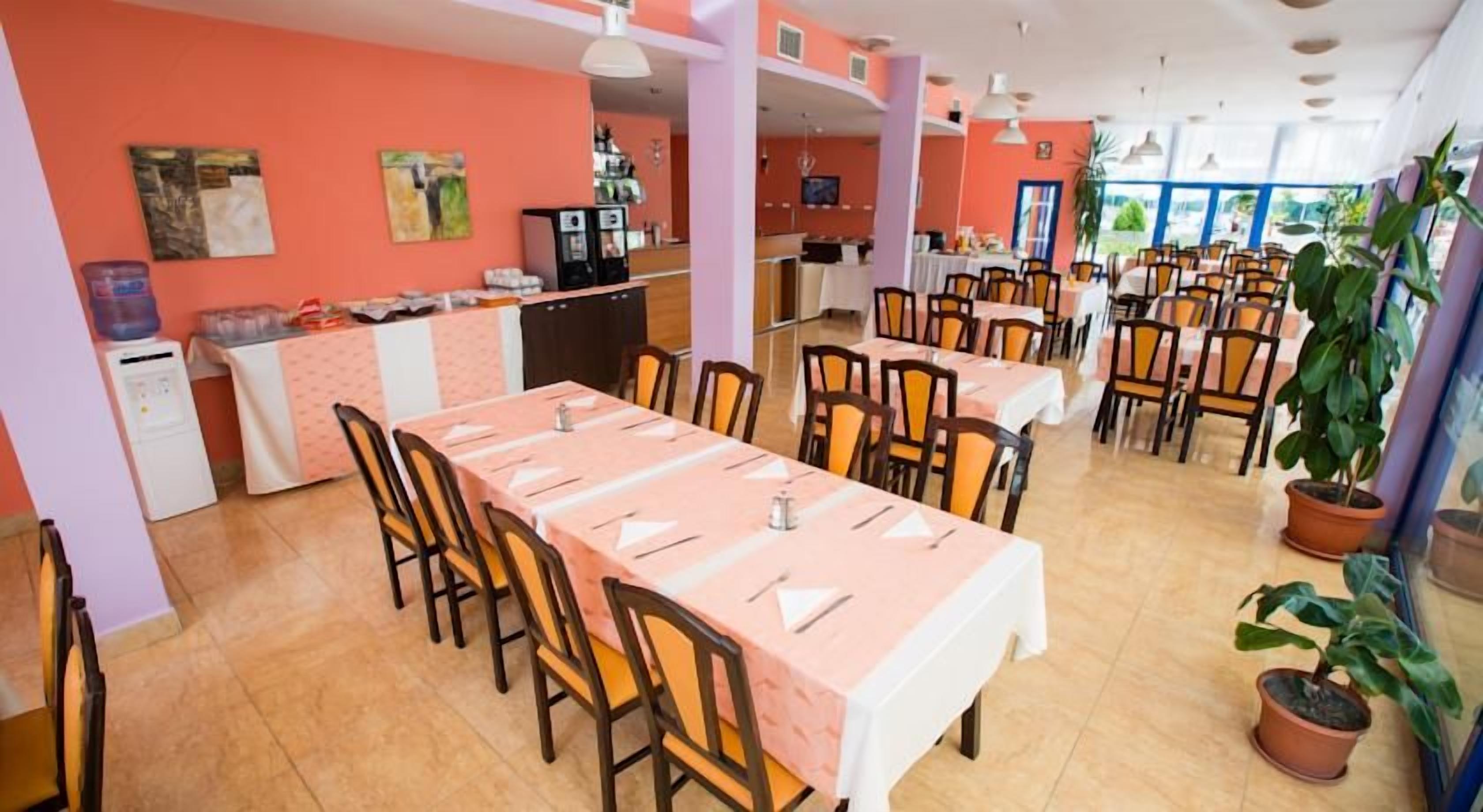 Un comedor con mesas dispuestas para varias personas, una zona de cocina y una barra con dispensador de agua.