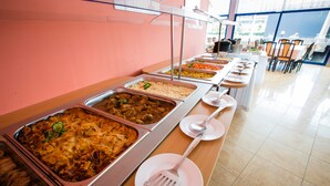 Een buffet met diverse stations, waaronder pasta, rijst en verschillende gerechten, in een goed verlichte kamer met betegelde vloer.