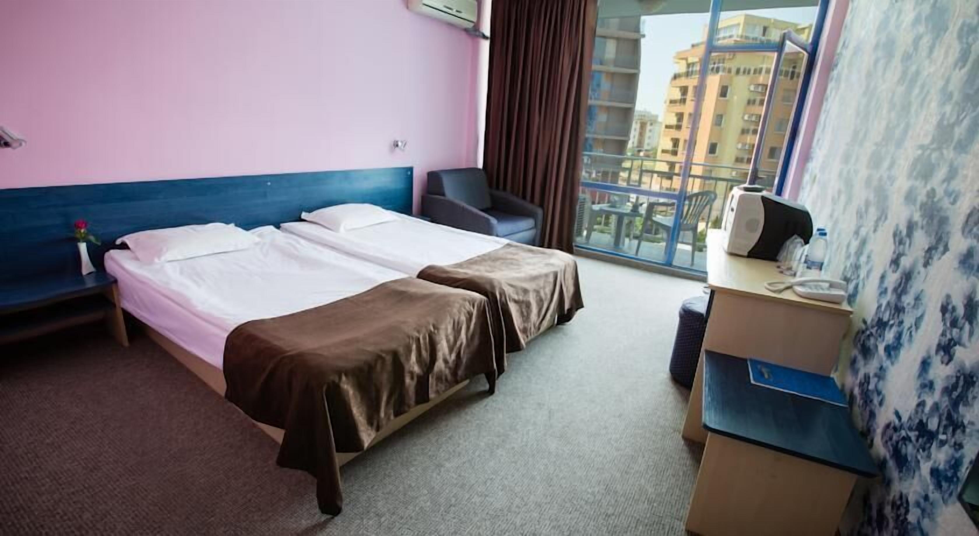 A hotel room with two beds, a desk, and a window with a city view.
