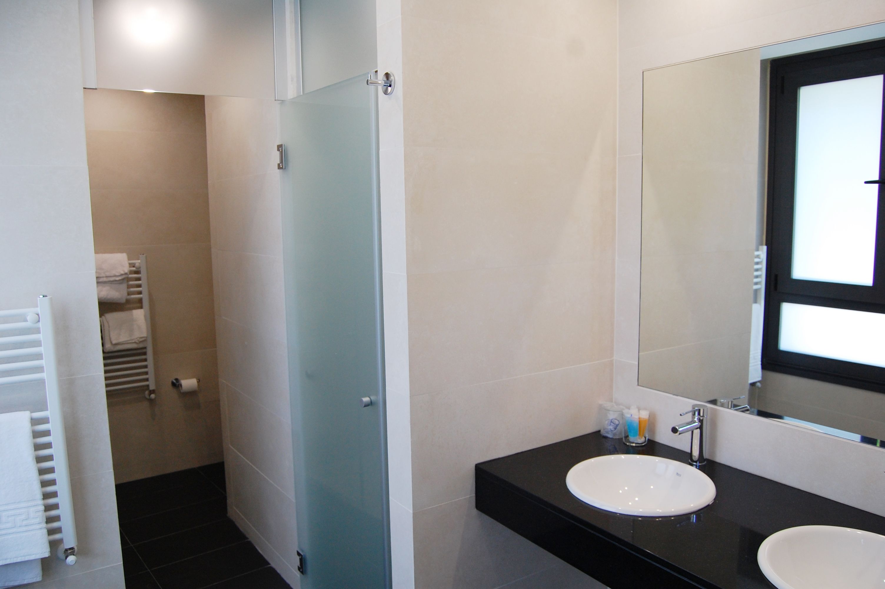 Un baño moderno con un lavamanos blanco, un espejo grande y una puerta de ducha de cristal.
