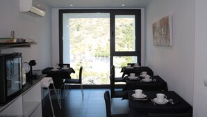 Een moderne eethoek met tafels voor twee personen, een koelkast en een groot raam met uitzicht op de omgeving.