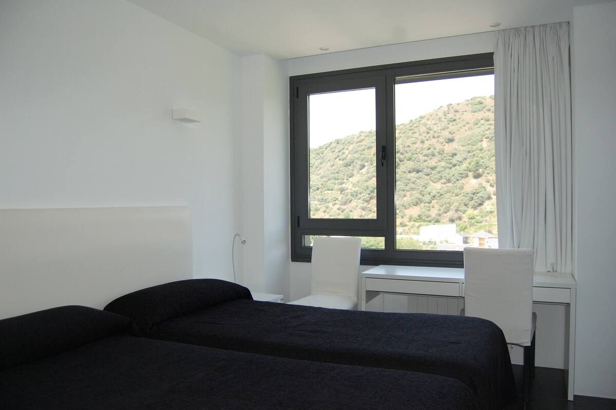 Een hotelkamer met een bed, een bureau en een stoel. Er is een raam met uitzicht op een glooiend landschap.