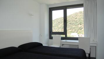 Een hotelkamer met een bed, een bureau en een stoel. Er is een raam met uitzicht op een glooiend landschap.