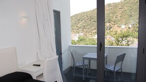 Een balkon met een tafel en stoelen, een wit bureau en uitzicht op een heuvel.