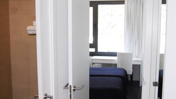 Quarto de hotel com cama, escrivaninha e janela com cortinas.