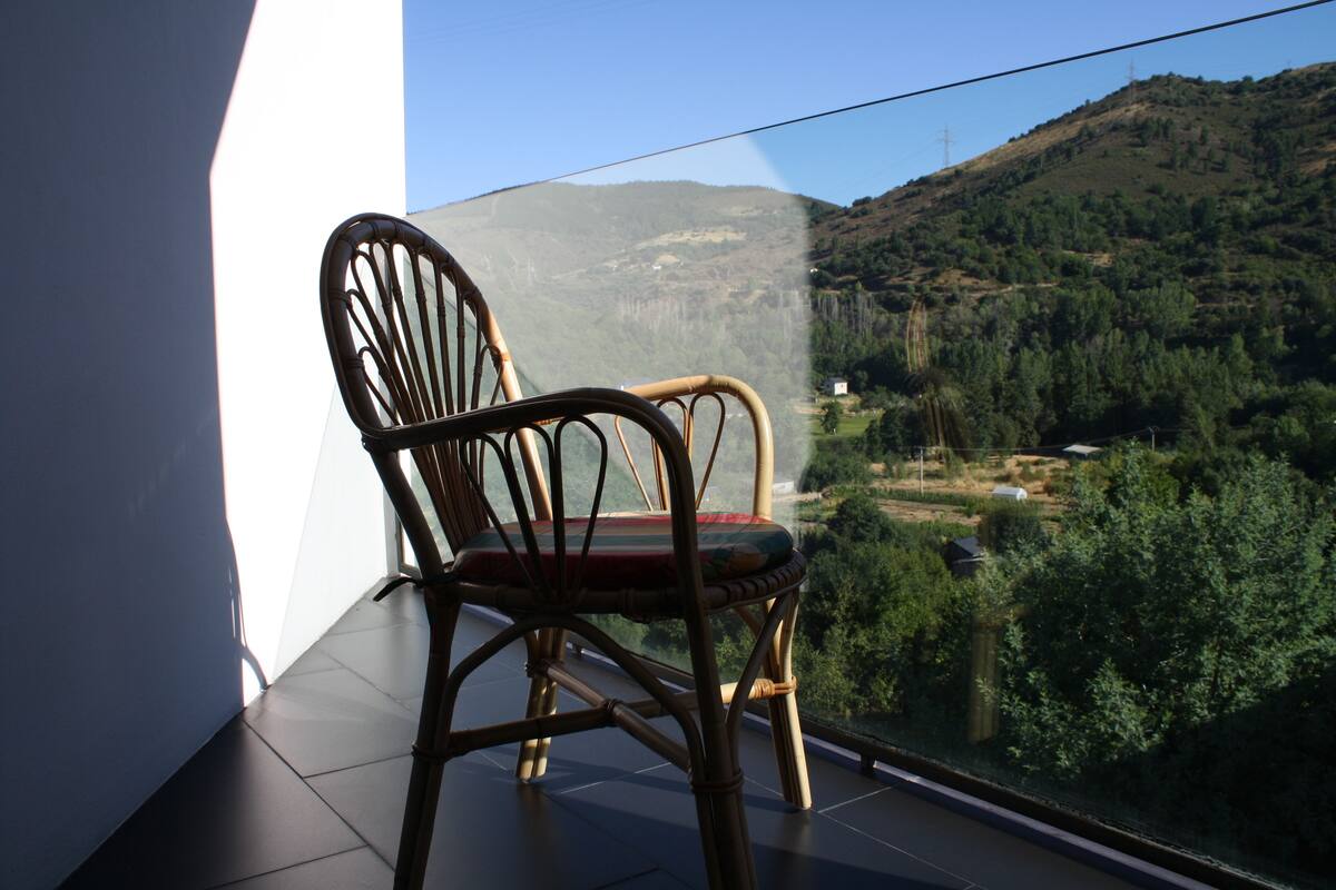 Een rieten stoel op een balkon met uitzicht op een bergachtig landschap.