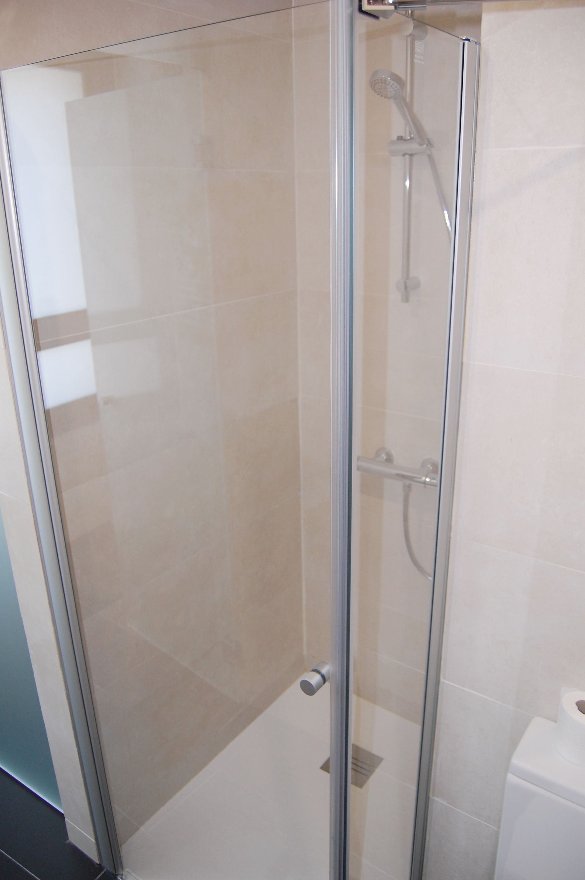A glass-enclosed shower stall with a handheld showerhead and a wall-mounted faucet.