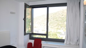 Een kamer met een bed, een bureau en een raam met uitzicht op een heuvelachtig landschap.