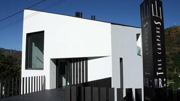 A modern building with a white facade, a large window, and a sign reading "Tres Campanas."