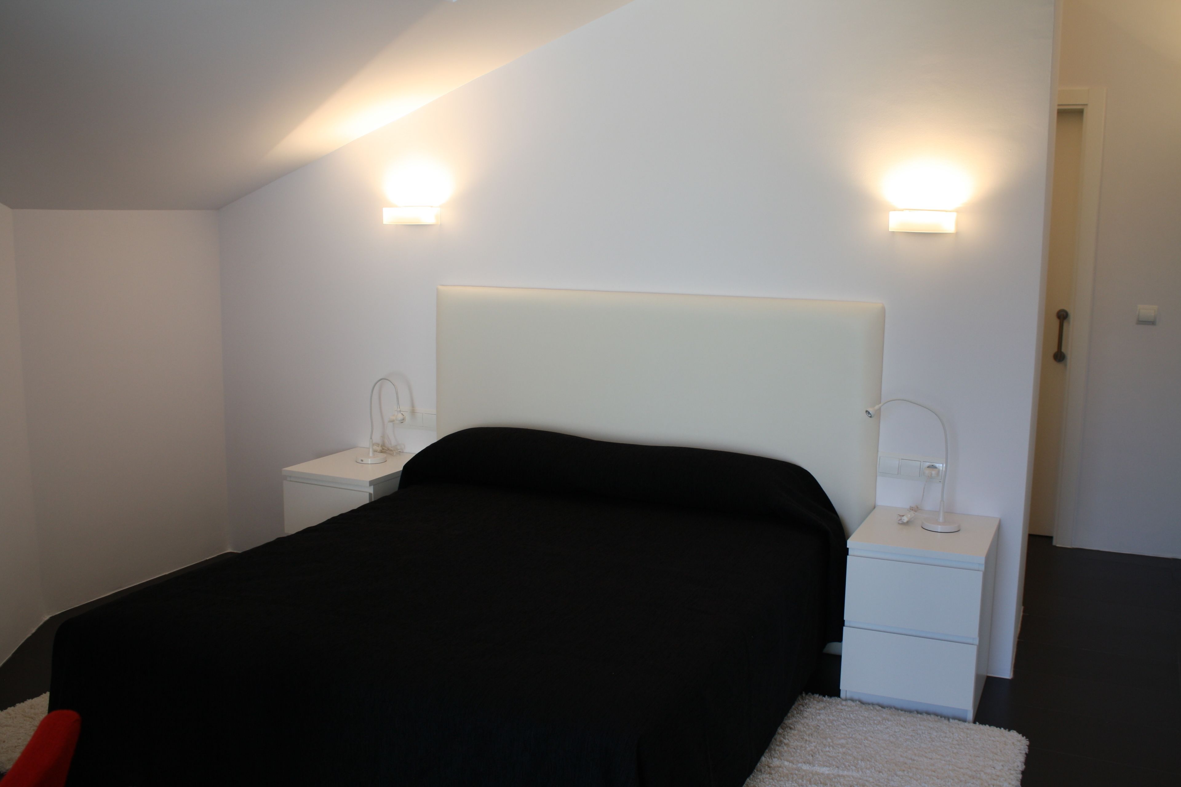 Un dormitorio moderno con una cama grande, mesitas de noche y luces fijadas a la pared.