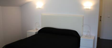 A modern bedroom with a large bed, bedside tables, and wall-mounted lights.