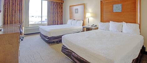 A hotel room with two beds, a desk, a chair, a lamp, and a window with curtains.