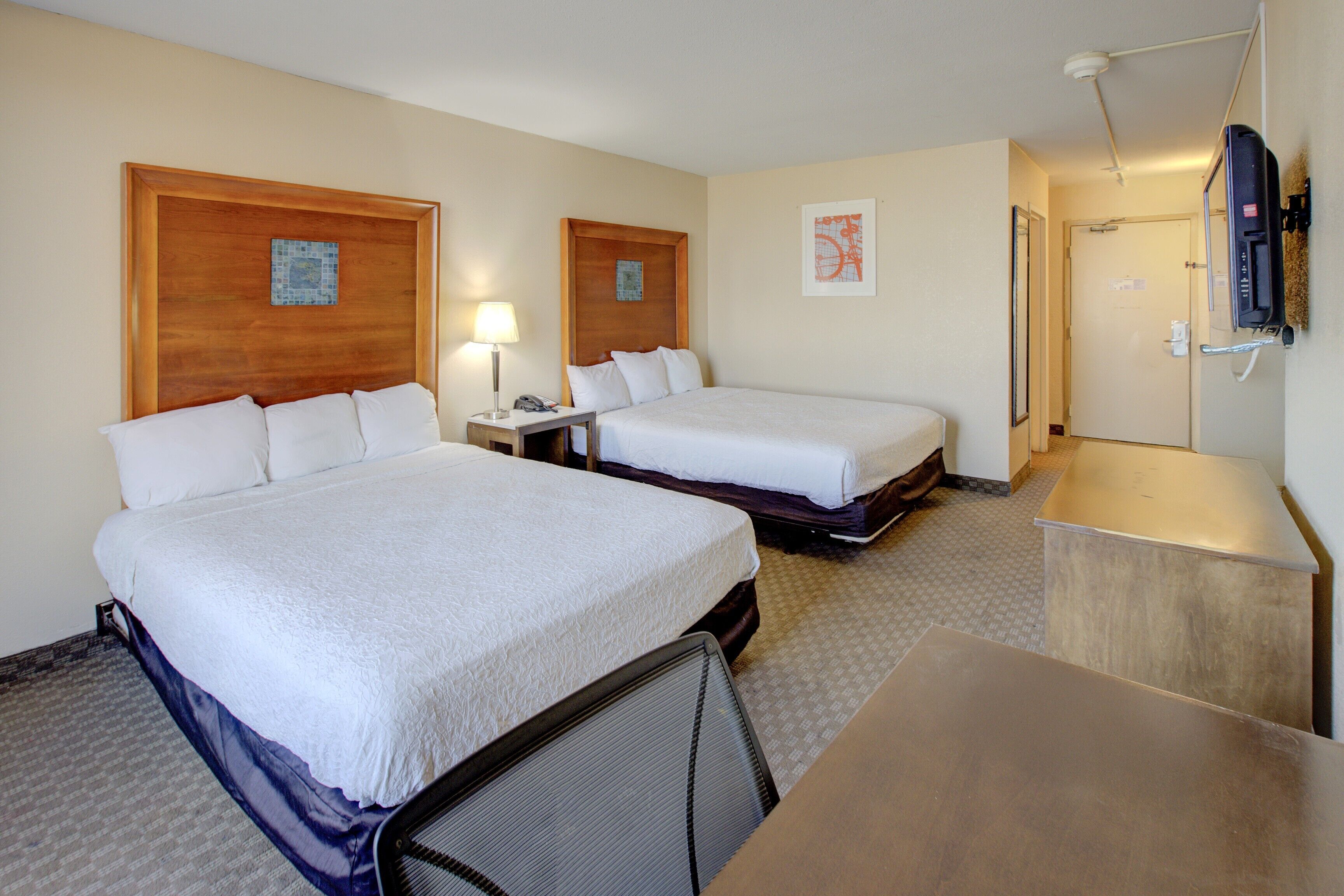 Ett hotellrum med två sängar, ett skrivbord, en stol, en tv och en dörr till badrummet.