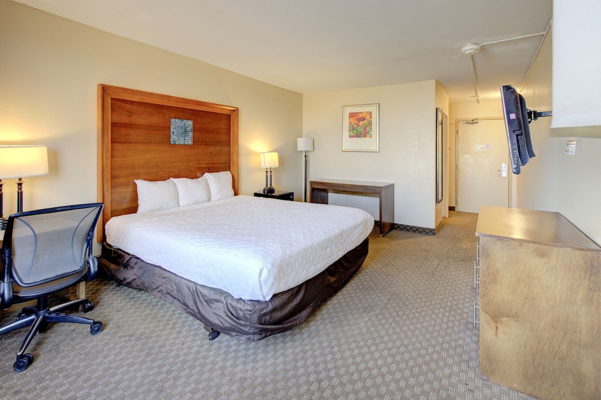 A hotel room with a large bed, a desk, a chair, a desk lamp, a picture on the wall, and a television mounted on the wall.