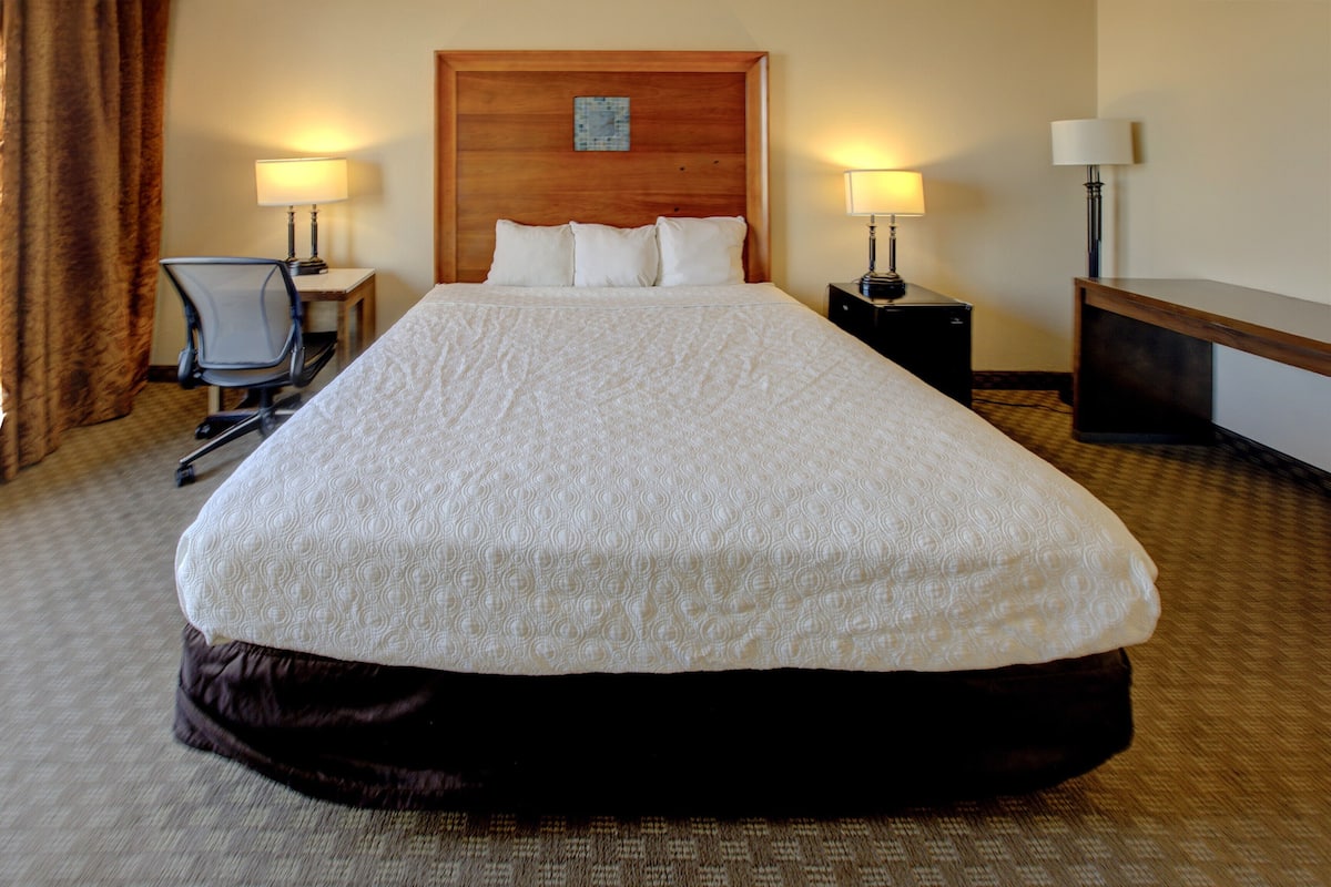 A hotel room with a large bed, two bedside tables with lamps, a chair, and a wooden headboard.