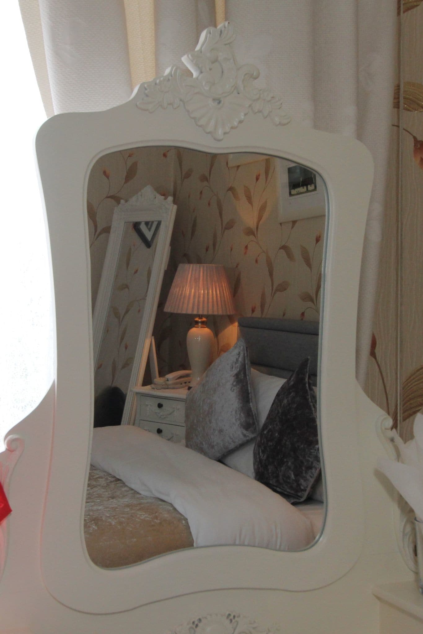 Un dormitorio con cama, mesita de noche, lámpara y espejo.