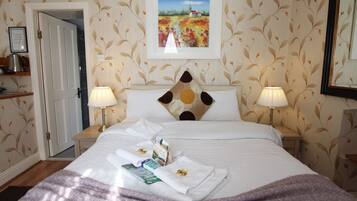 A hotel room with a bed, two bedside lamps, a framed painting above the bed, and a door leading to another room.