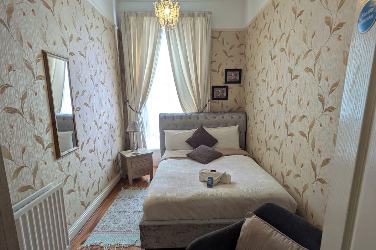 A bedroom with a bed, a nightstand, a dresser, a chair, and a chandelier.