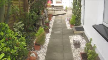 Un étroit sentier bordé de plantes en pot mène à l’entrée d’un bâtiment.