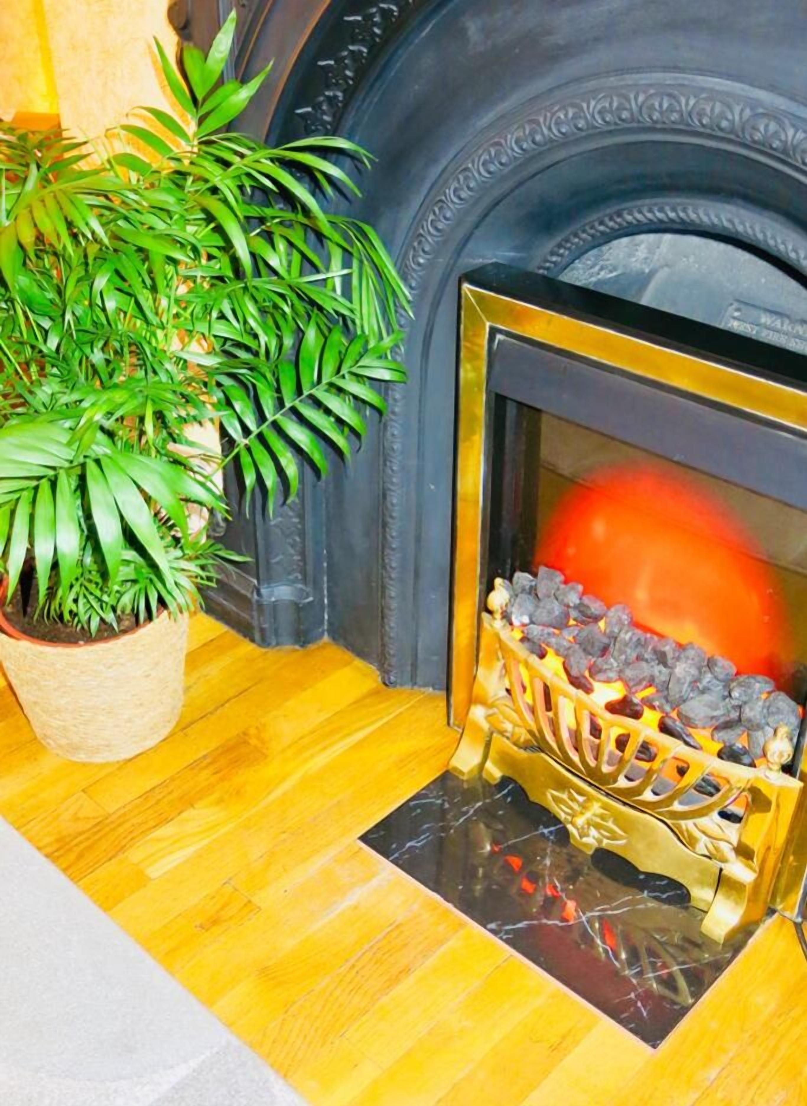 Una chimenea con un celosía decorativa, una planta en maceta y piso de madera.