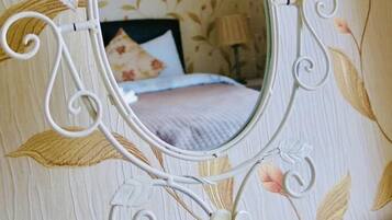 Un espejo con marco floral en una habitación con papel tapiz de motivos florales.