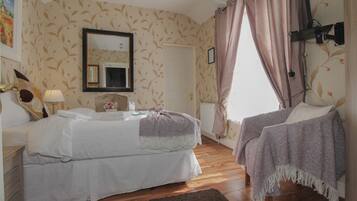 A bedroom with a double bed, a bedside table, a nightstand, a dresser, a mirror, a window with curtains, and a radiator.
