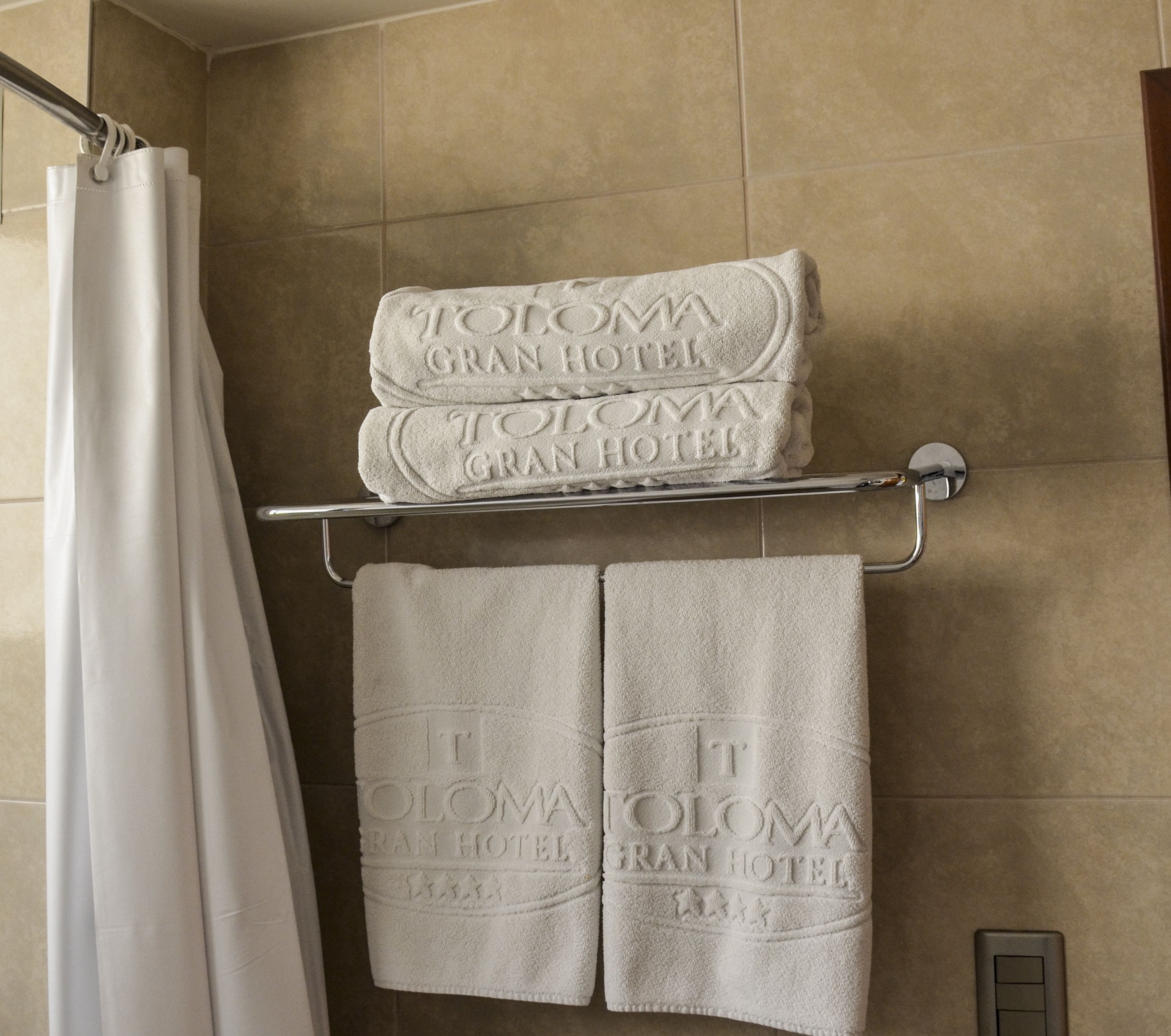 A bathroom with a shower curtain, a towel rack holding two folded towels, and a towel rack with two towels.