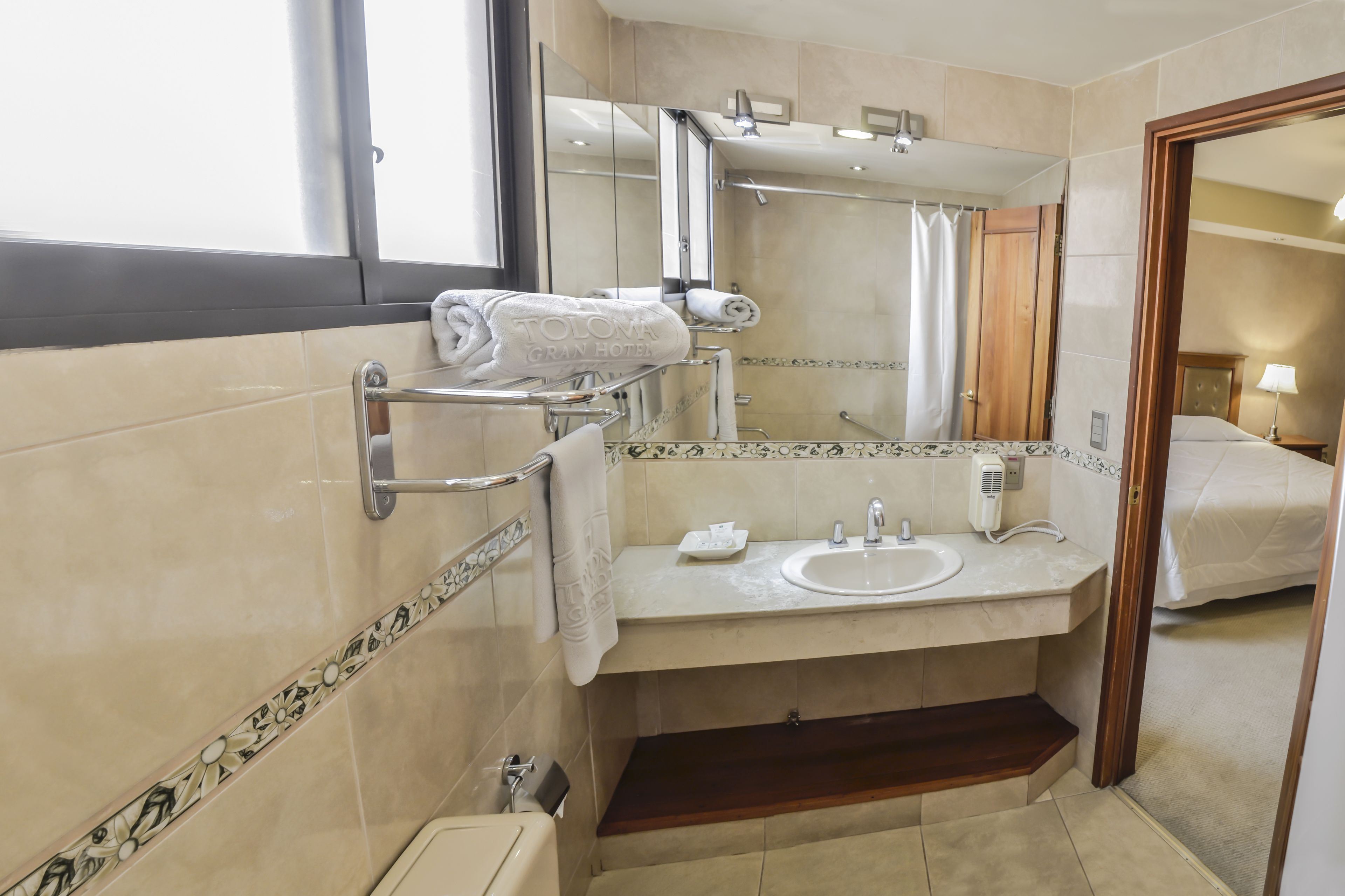 A hotel bathroom with a sink, mirror, towel rack, and shower area.
