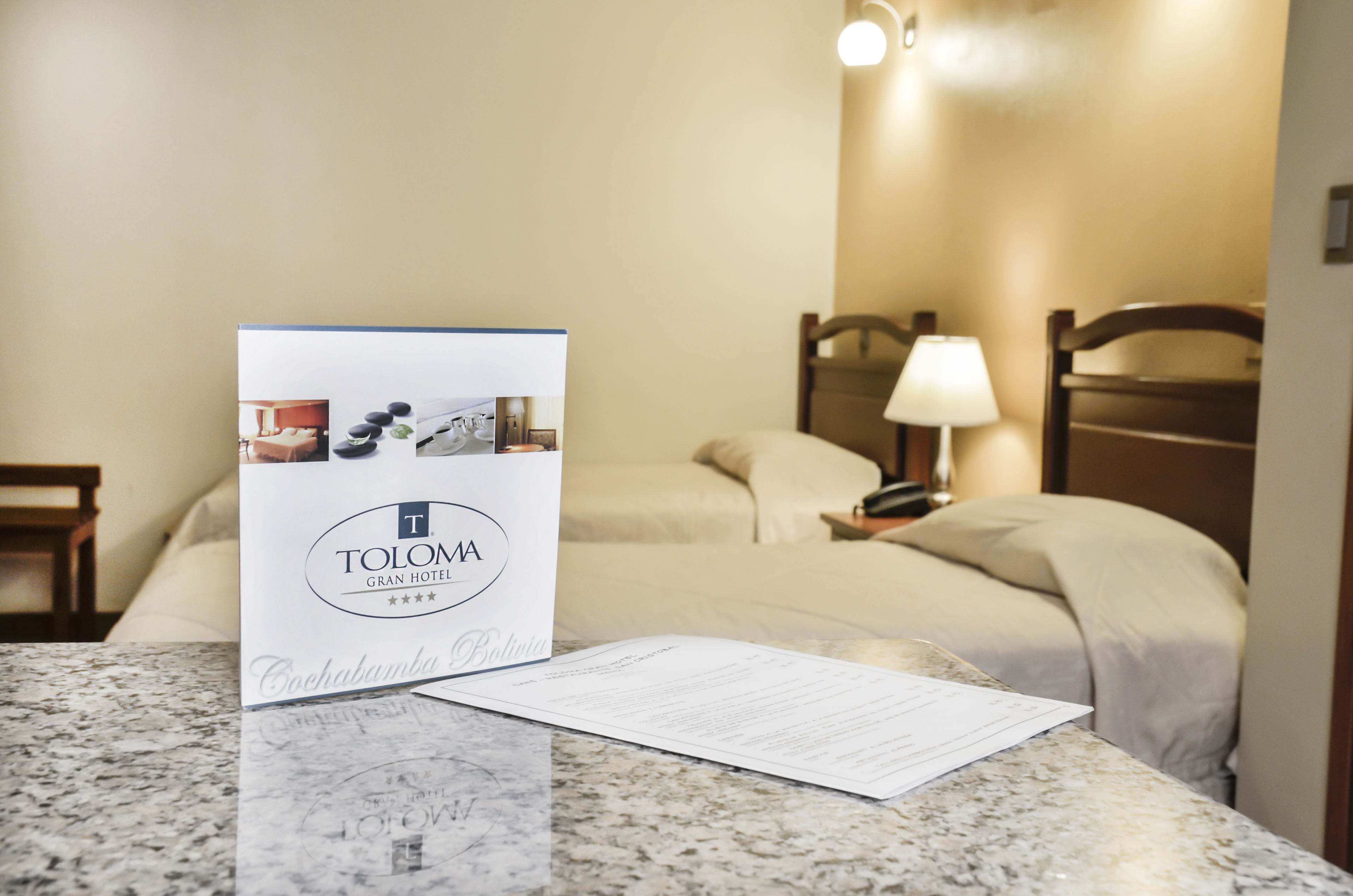 A hotel room with a bed, a nightstand, a lamp, and a brochure on the table.