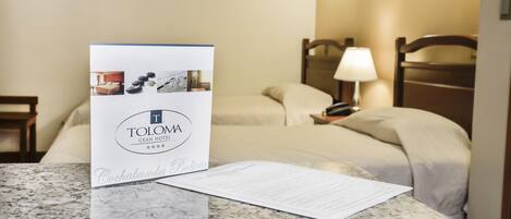 A hotel room with a bed, a nightstand, a lamp, and a brochure on the table.