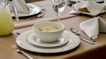 A dining table set with a bowl of soup, a glass of water, a pitcher of a yellow beverage, and cutlery.
