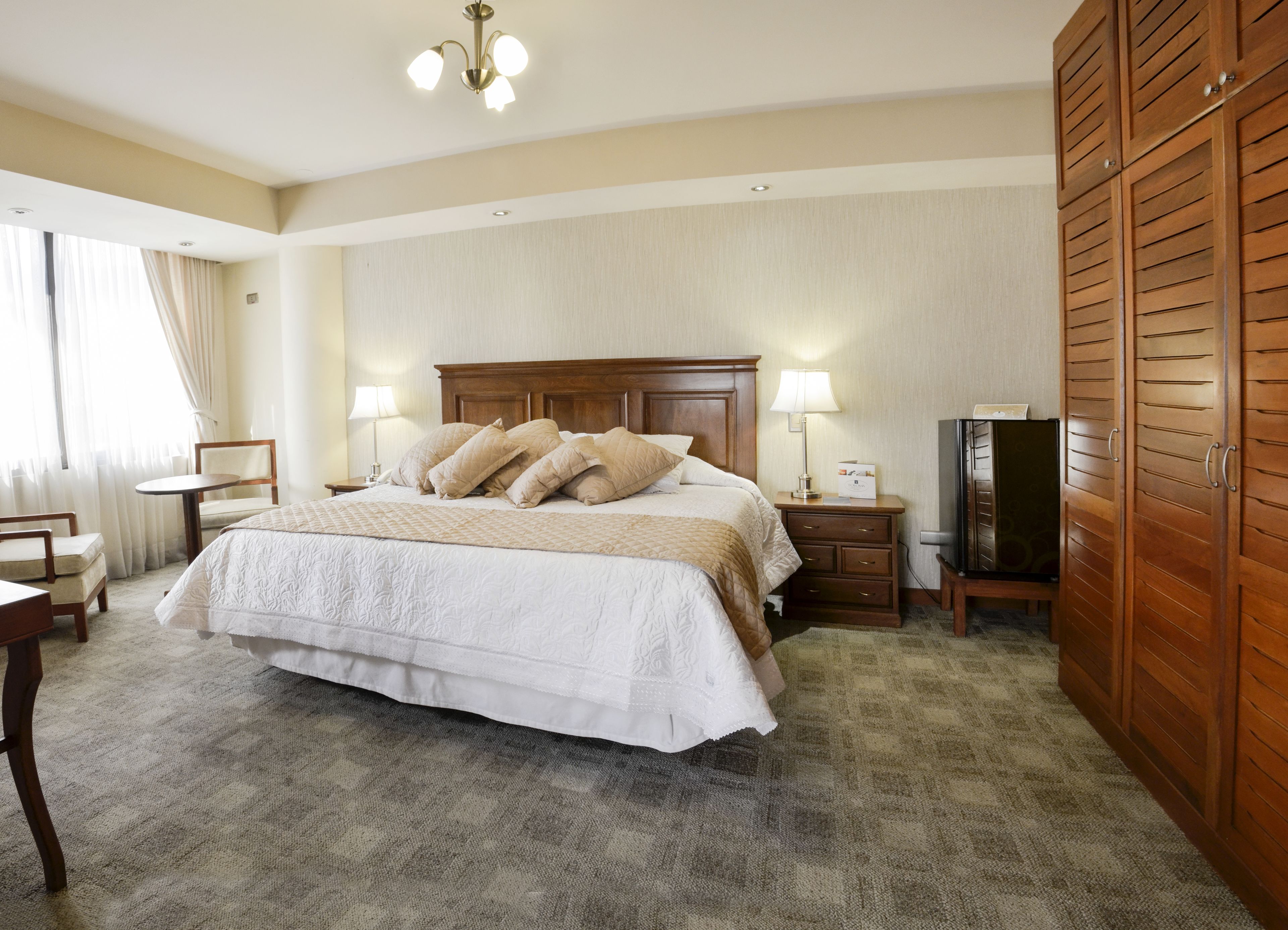 Une chambre d’hôtel avec un grand lit, deux tables de chevet, une télévision, une armoire et un bureau avec une chaise.