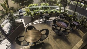 An outdoor seating area with round tables and chairs, surrounded by potted plants and a view of the street. - Gran Hotel Toloma (Cochabamba)