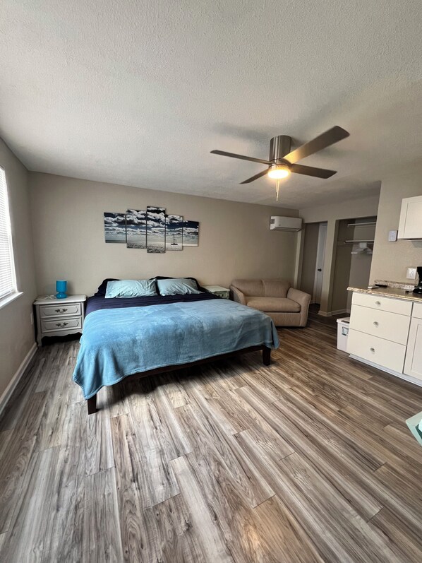 A bedroom with a bed, a ceiling fan, a nightstand, a dresser, and a window. - Serenity Bay Cottages (Matlacha)