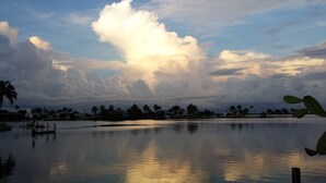 Um lago tranquilo com reflexos de nuvens, rodeado por palmeiras e casas.