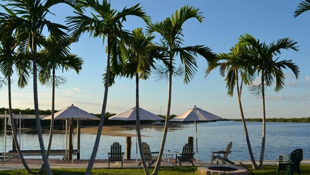 Um terraço à beira do lago com cadeiras de descanso, guarda-sóis e um cais.